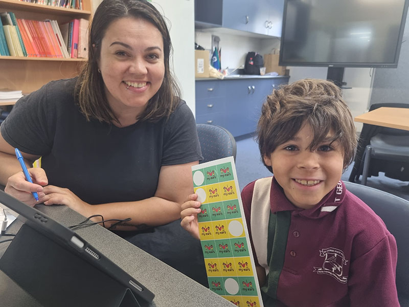 Photo of a teacher and student sitting down in front of a tablet in a school office.