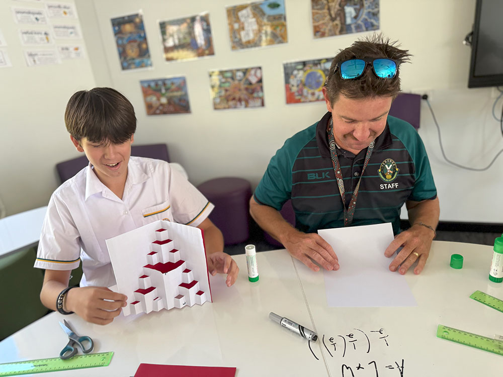 Students fold and cut paper to create repeating patterns resembling the Sierpinski triangle