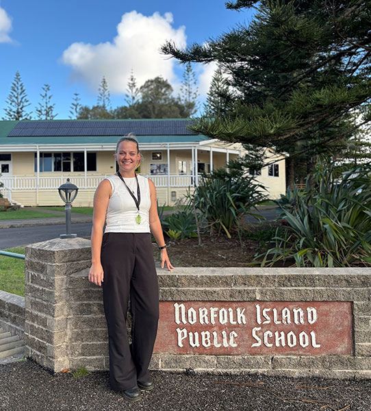 Kristin Ellard standing in front of signage saying 'Norfolk Island Public School'