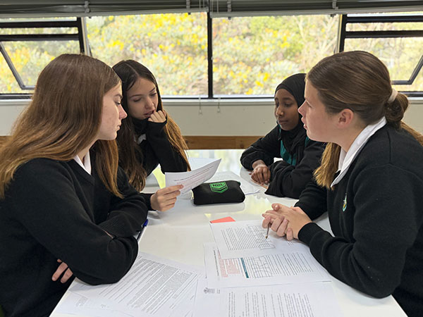 Four students engaged in a discussion while seated around a table.