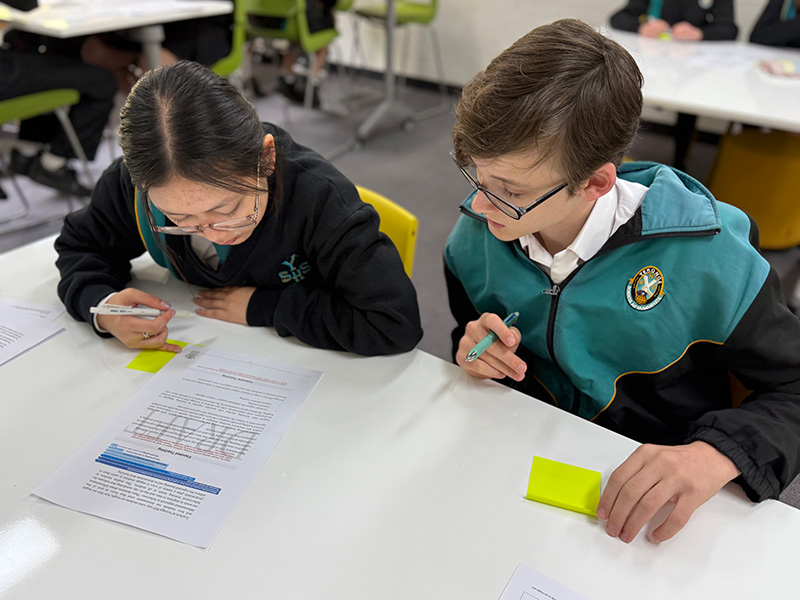 Two students collaborating with a document on the table, each with a sticky notes pad in front of them.