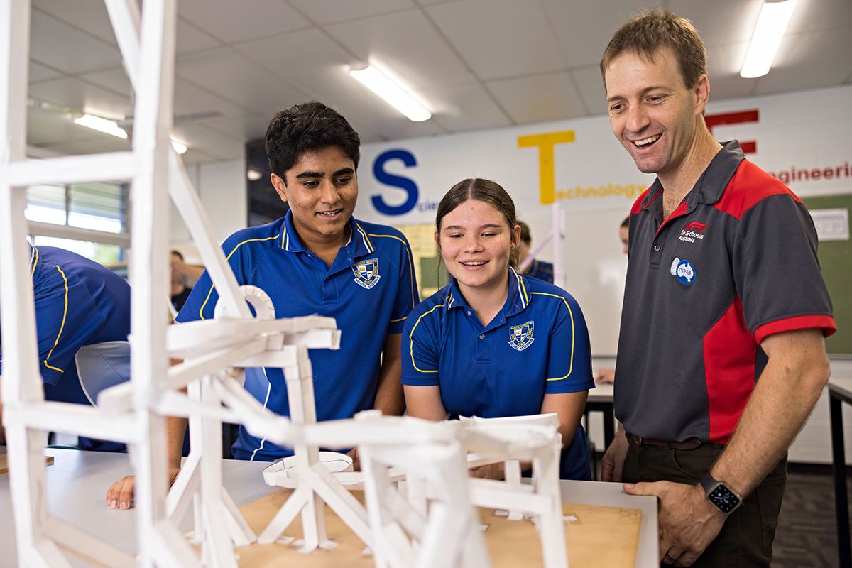 An adult and 2 students gather around a desk in a classroom setting, engaged in an activity together.